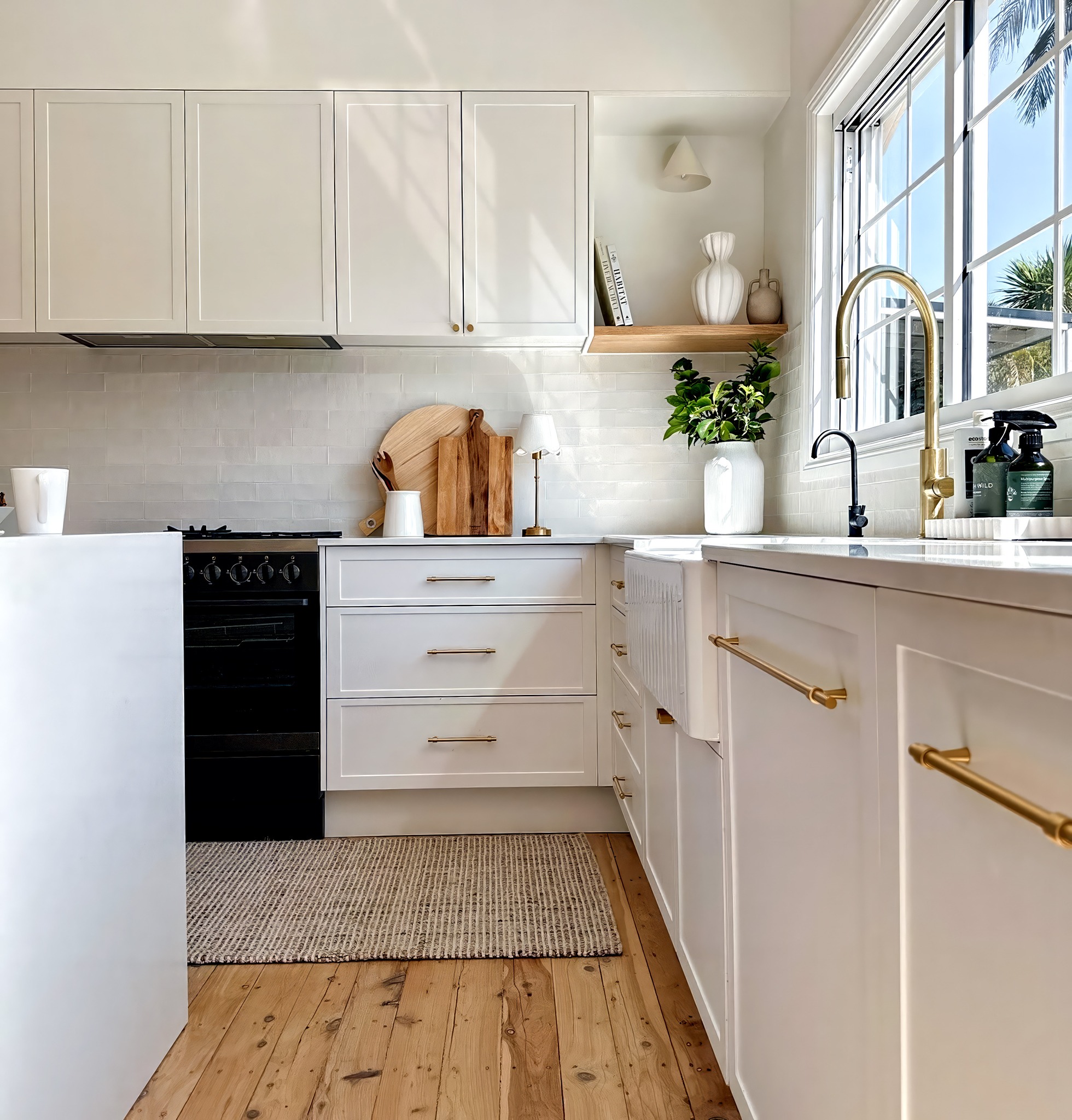 White shaker cabinets with brass bar pulls, white farmhouse sink, white handmade subway tile backsplash, brass pull-down faucet, and wide pine plank flooring