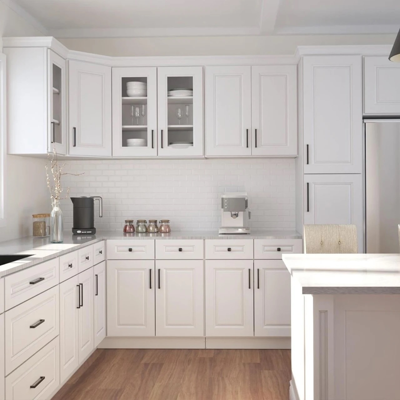 Classic white raised panel kitchen cabinets with glass-front uppers displaying dishware, dark bronze bar pulls, white brick-style subway tile backsplash, and medium wood plank flooring