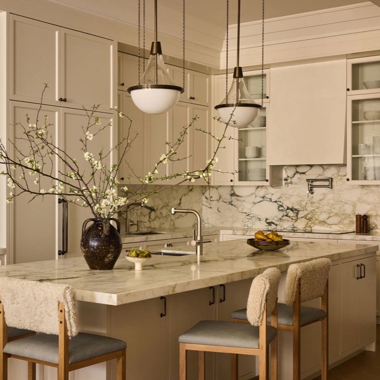 Soft beige cabinets with dramatic Calacatta Viola marble backsplash, pendant lights with white glass orbs, and boucle covered bar stools at the island