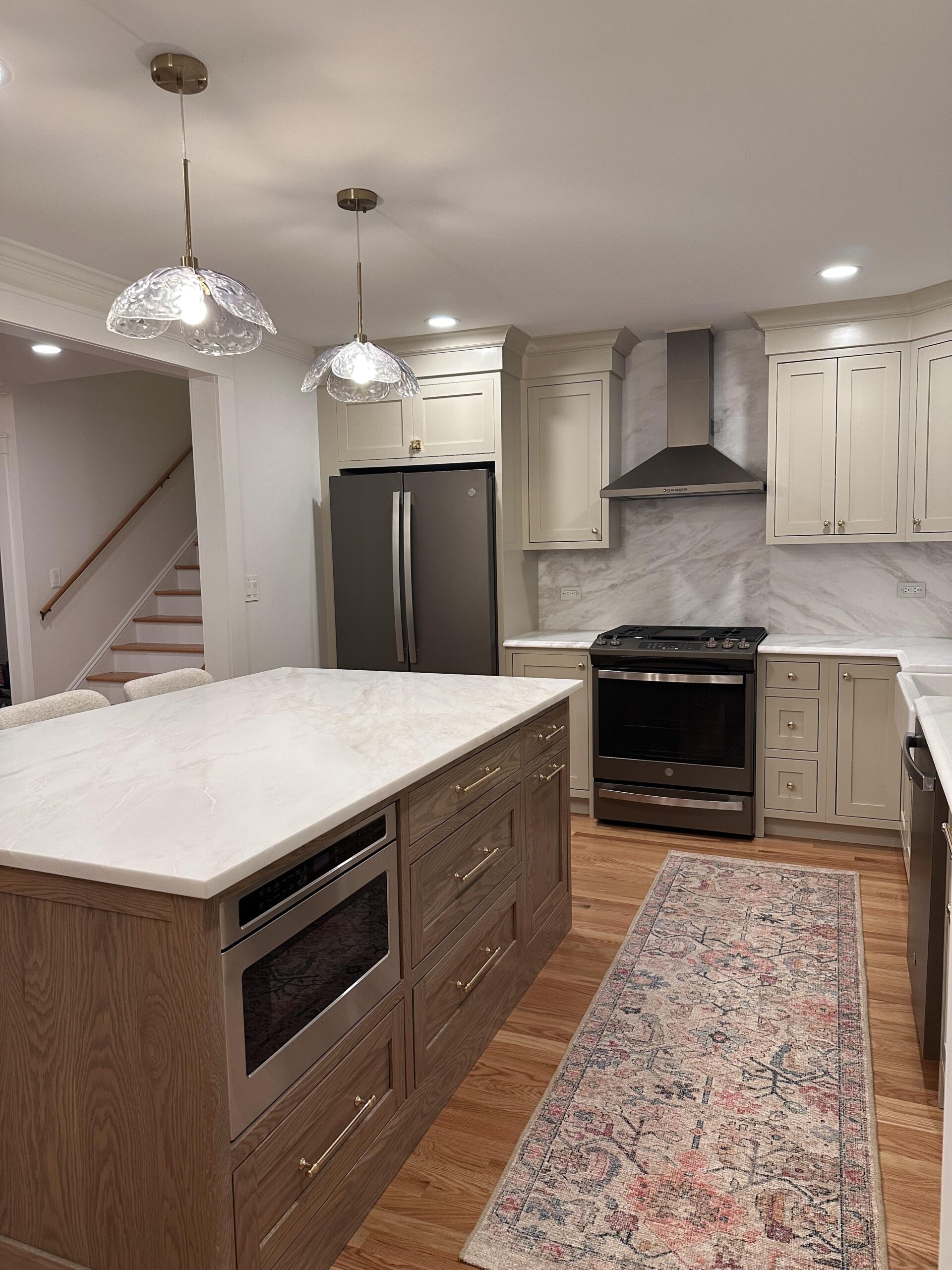 Kitchen with full-height Bianco Namibia marble backsplash behind a slide-in range, stainless chimney hood, and taupe shaker cabinets with brass knobs.