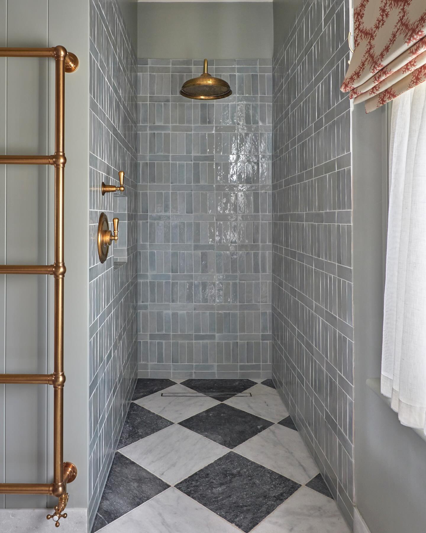 Narrow walk-in shower lined in dusty blue stacked zellige tiles with aged brass rainfall shower, two brass lever handles, a shiplap side wall, and a black and white marble checkerboard floor