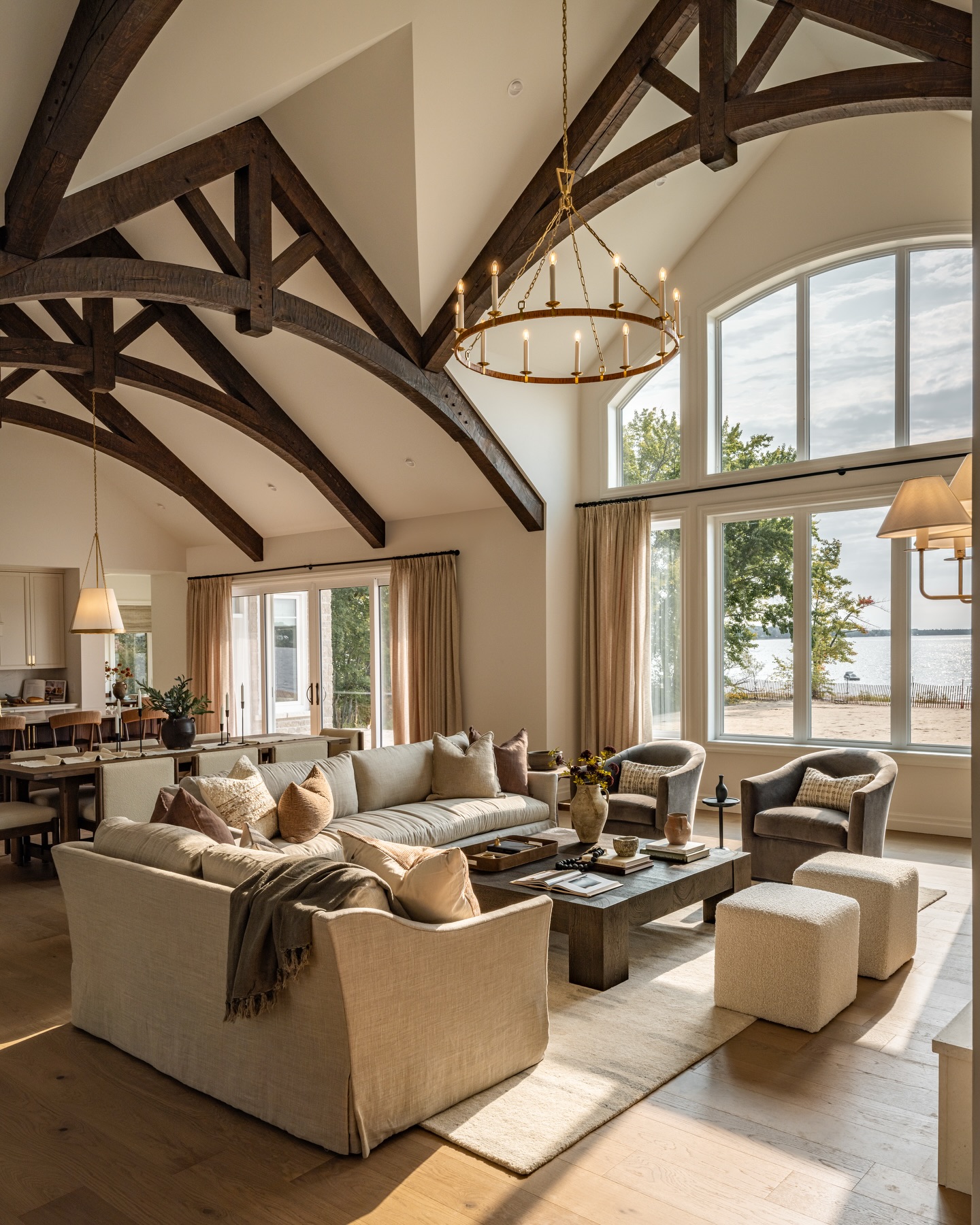 Modern farmhouse great room with cathedral ceiling, dark wood trusses, brass candle chandelier, and cream slipcovered sectional facing a large arched window