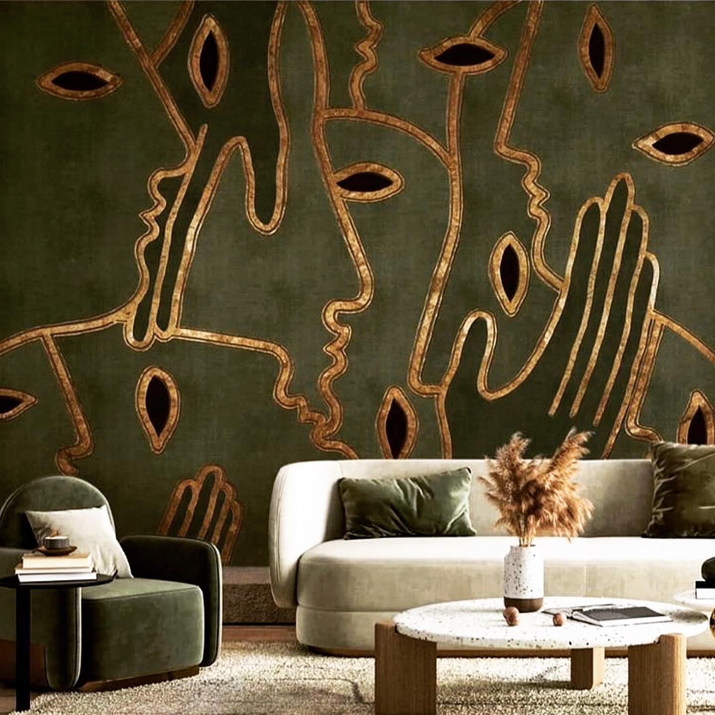 : Dark olive green wall mural with abstract gold line-drawn faces, eyes, and hands behind a cream curved sofa, with a dark green velvet armchair, pampas grass in a speckled vase, and a round terrazzo coffee table