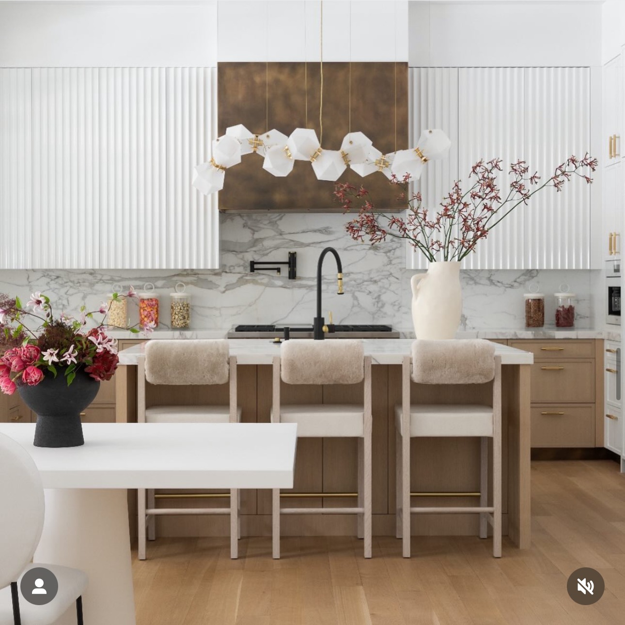 White fluted upper cabinets with a dramatic Calacatta marble backsplash, light wood lower cabinets, and shearling bar stools at the island