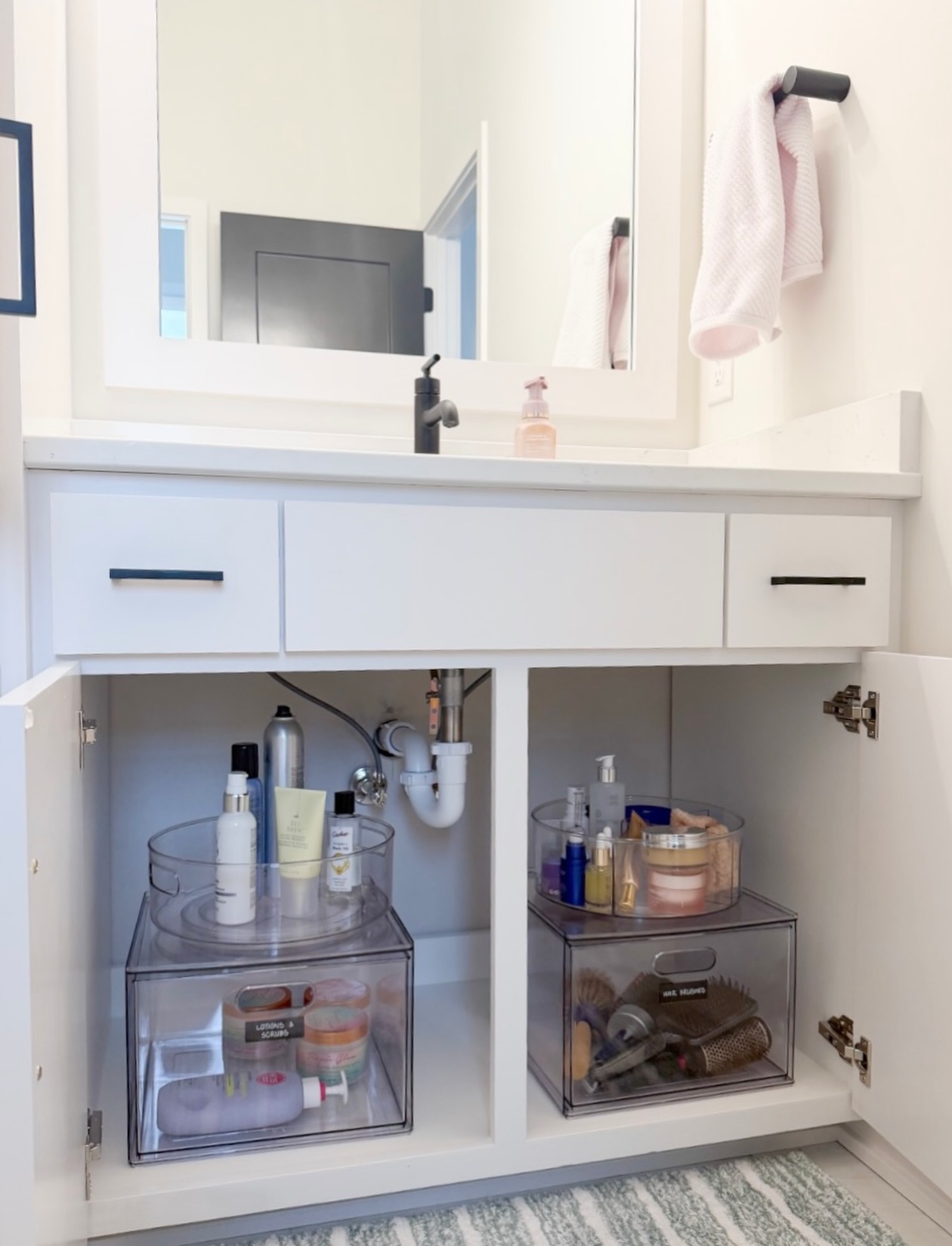 Open white bathroom vanity with two clear lazy susan turntables on top of two clear pull-out drawers, holding lotions and skincare on top with hair brushes and body scrubs in the drawers below