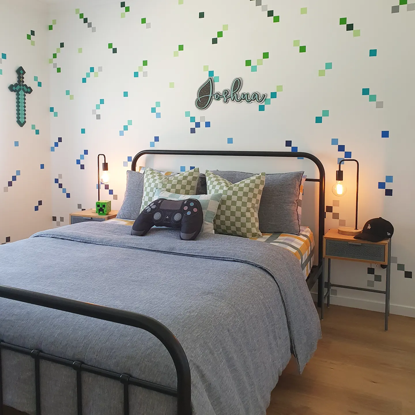 Minecraft inspired teen bedroom with scattered pixel confetti wall decals in green and blue black iron bed frame gray bedding and PlayStation controller pillow