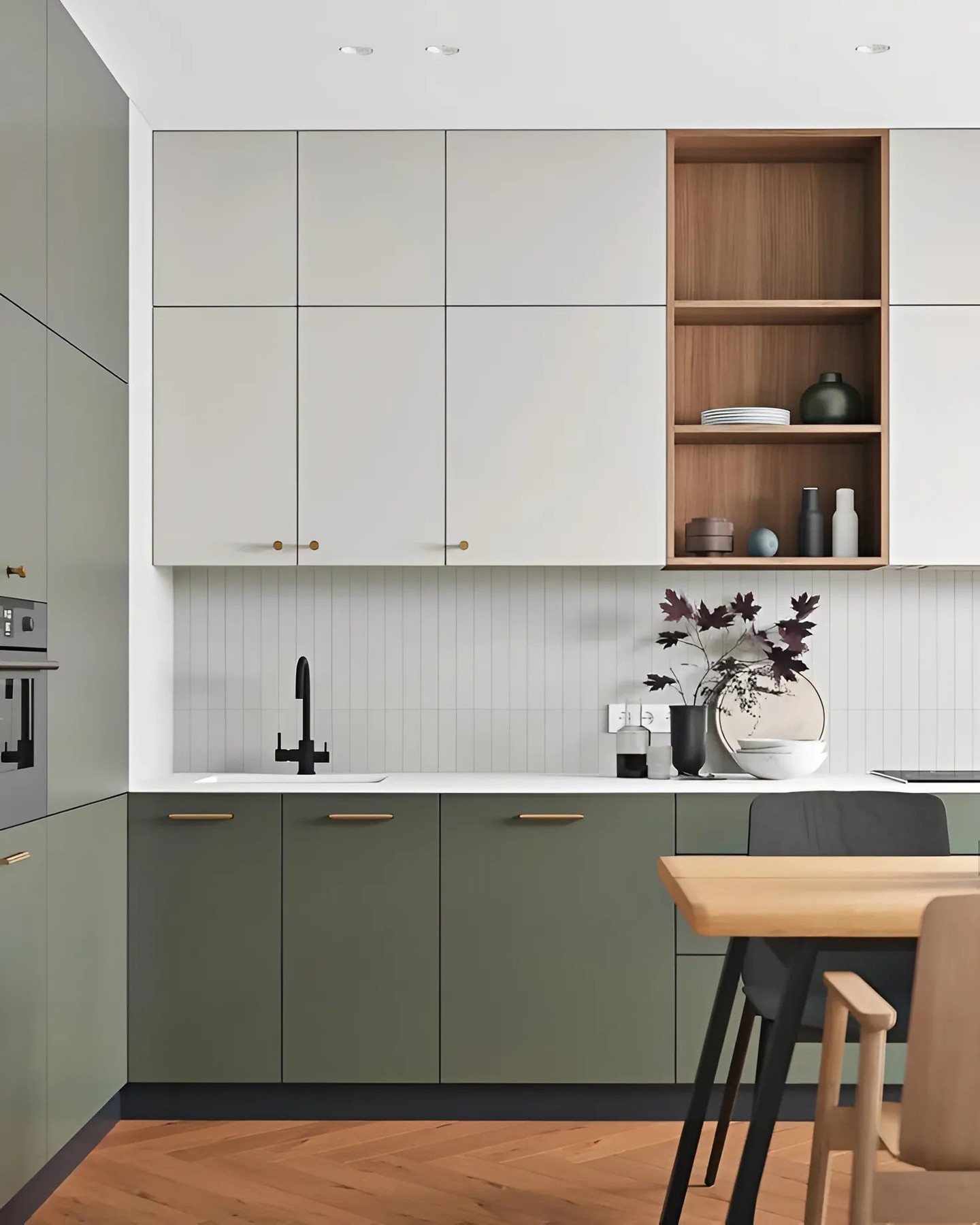 Modern two-tone kitchen with cream flat-front upper cabinets, olive green lower cabinets, open walnut shelving, a black two-handle faucet, and a herringbone wood floor
