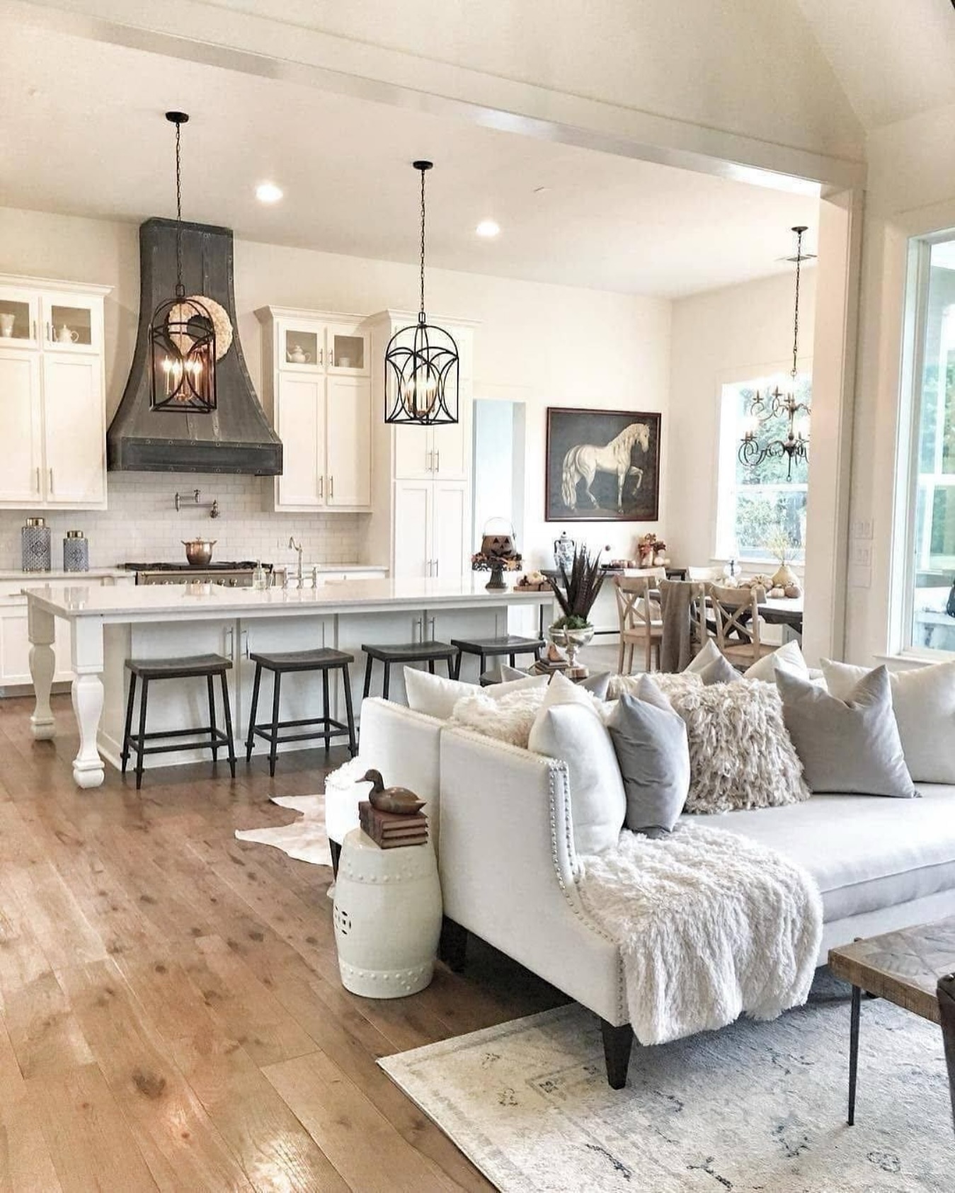 Open concept modern farmhouse living room with white studded sofa facing a white kitchen island, dark zinc range hood, and black iron lantern pendants over the island