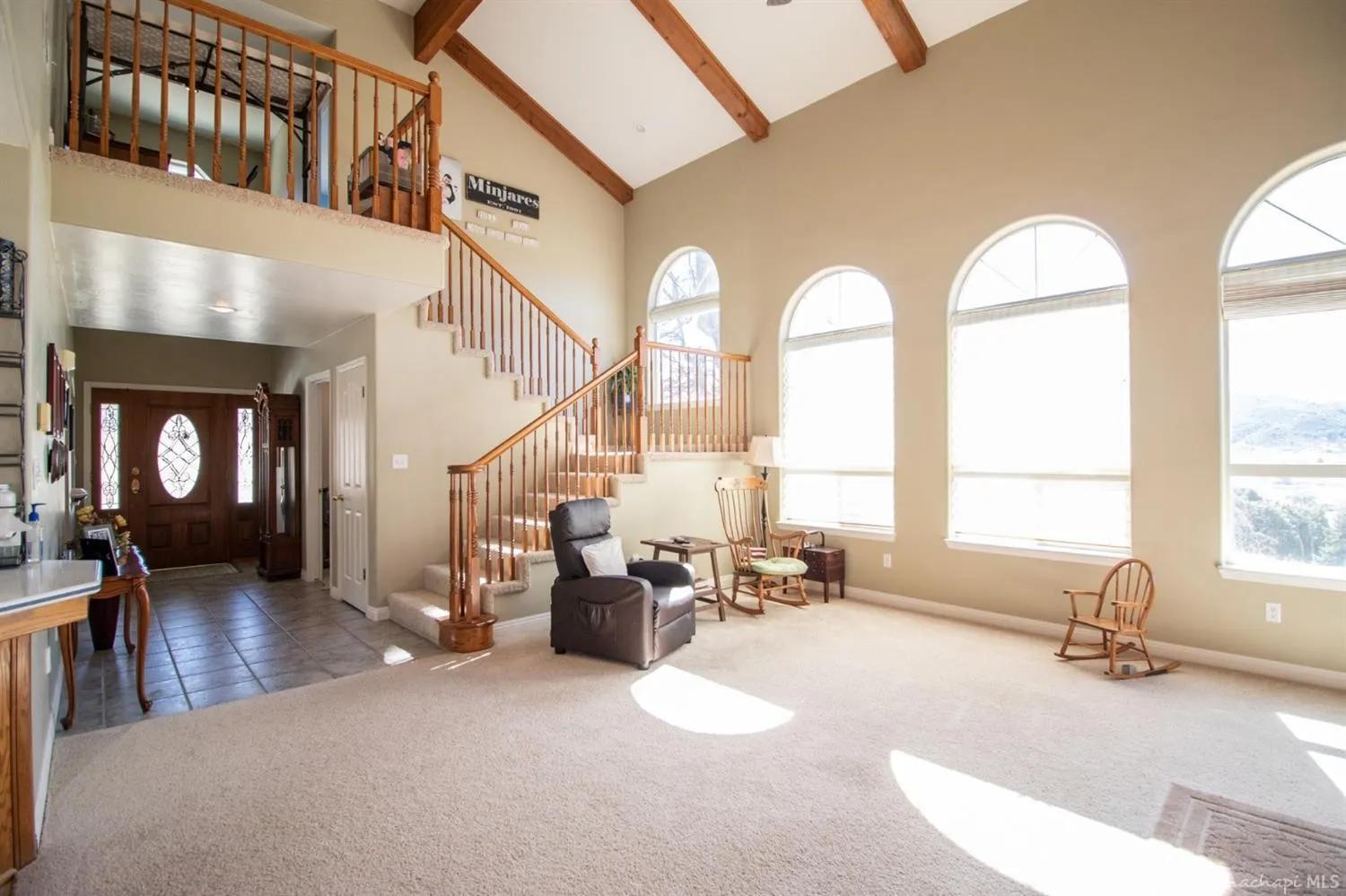 Original great room with high vaulted ceilings, exposed wood beams, oak railing, carpet, and an oak front door with an oval leaded glass insert and sidelights.