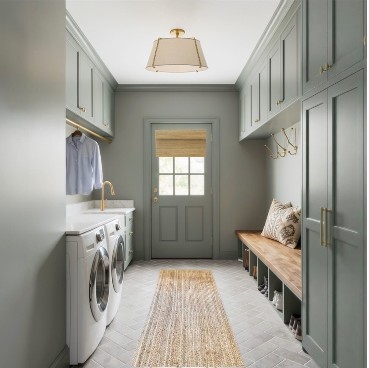 Narrow sage green mudroom laundry room with floor-to-ceiling cabinets, brass hardware, a wood bench with cubbies for shoes, a jute runner on herringbone tile, and a glass door at the far end