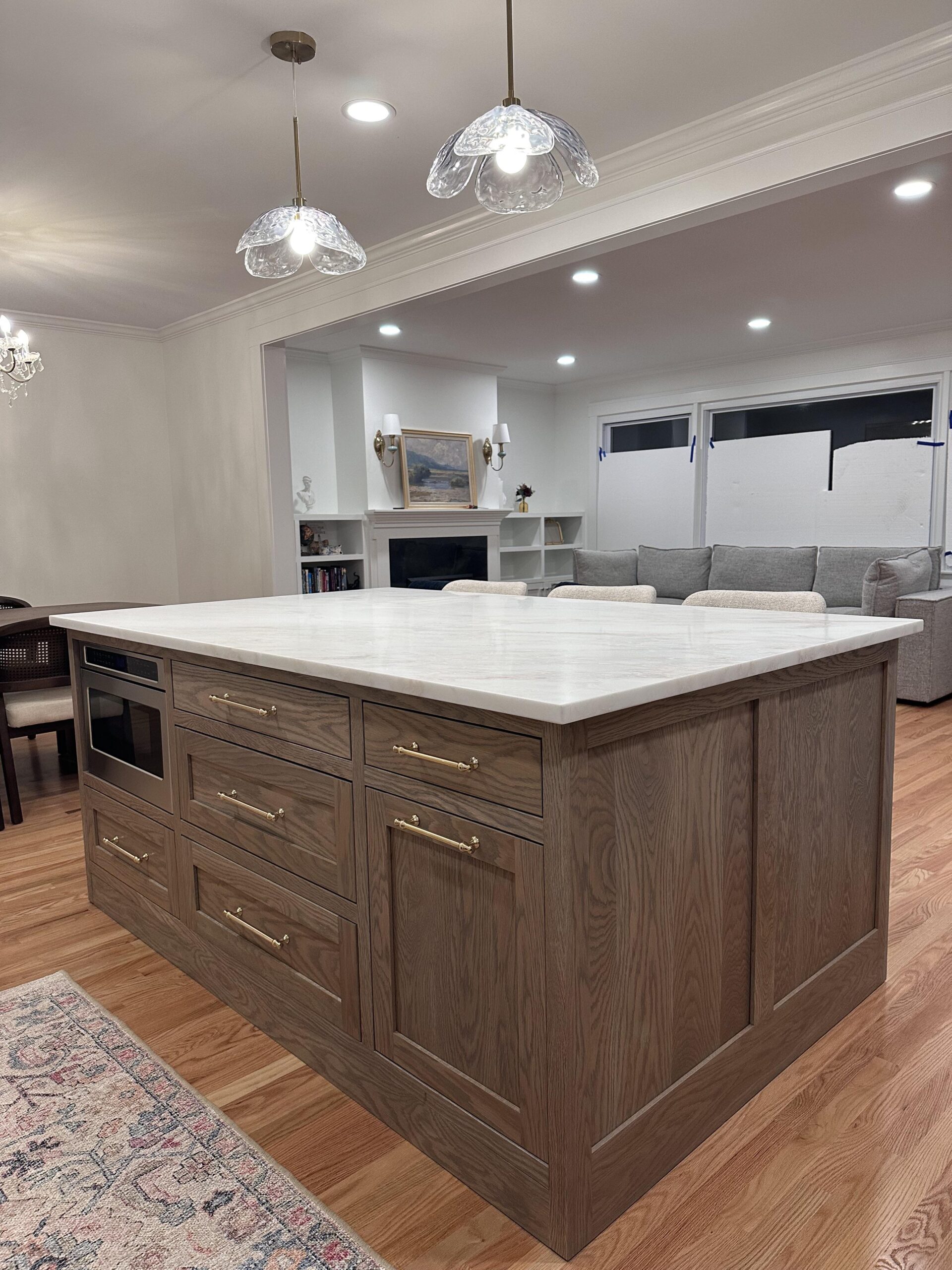 White marble island under two clear scalloped glass pendants with brass caps, faded red and blue vintage runner on hardwood floor, wood counter stools pulled up to the island.