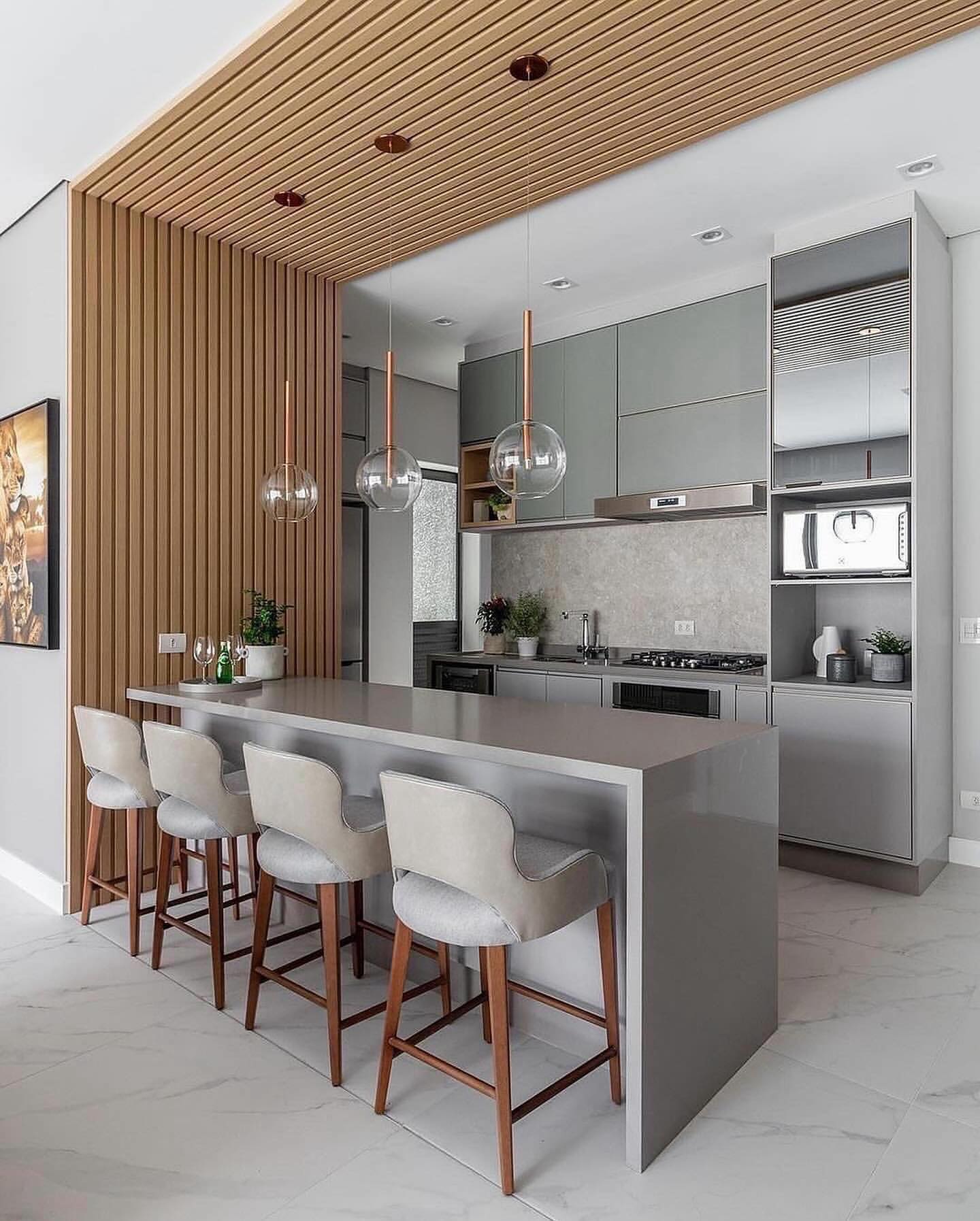 Slatted wood wall and ceiling panel framing an open kitchen with gray cabinets, a gray waterfall island, four cream bar stools, and three clear glass globe pendants