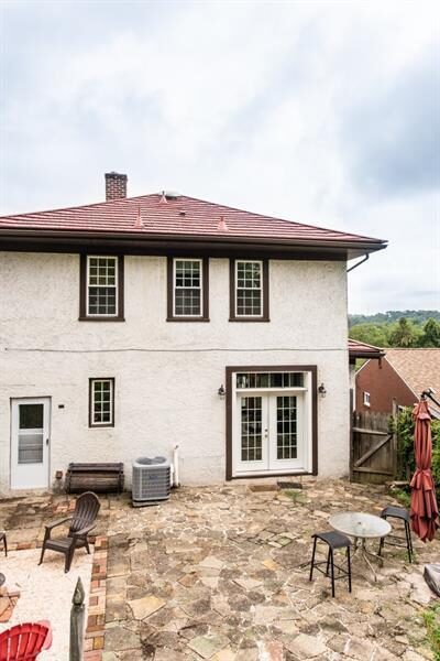 Back of a white stucco Spanish-style house with a red tile roof, cracked flagstone patio, a couple of Adirondack chairs, and a closed red umbrella.