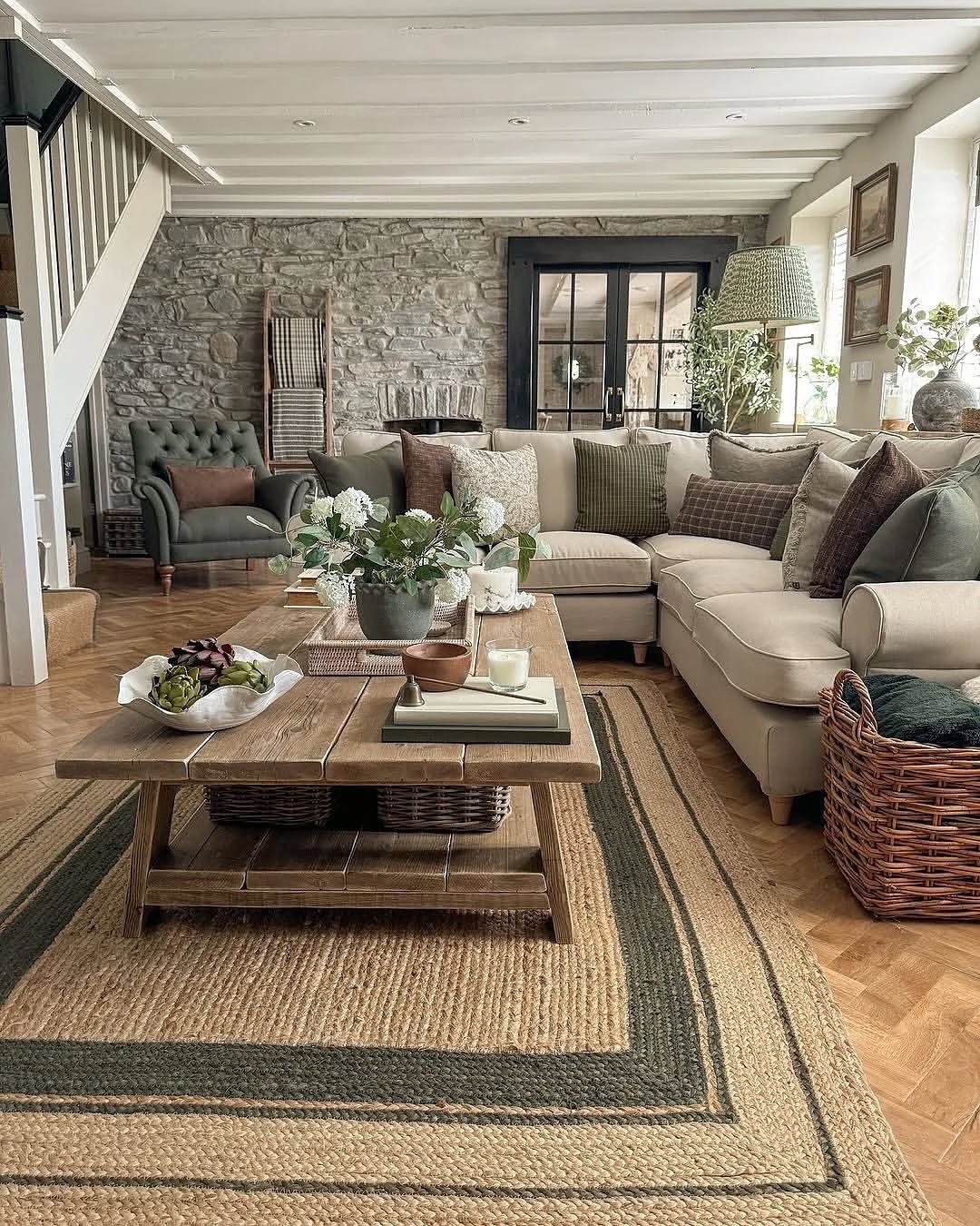 Cozy modern farmhouse living room with stone accent wall, cream sectional sofa, green velvet pillows, and bordered jute rug on parquet floor