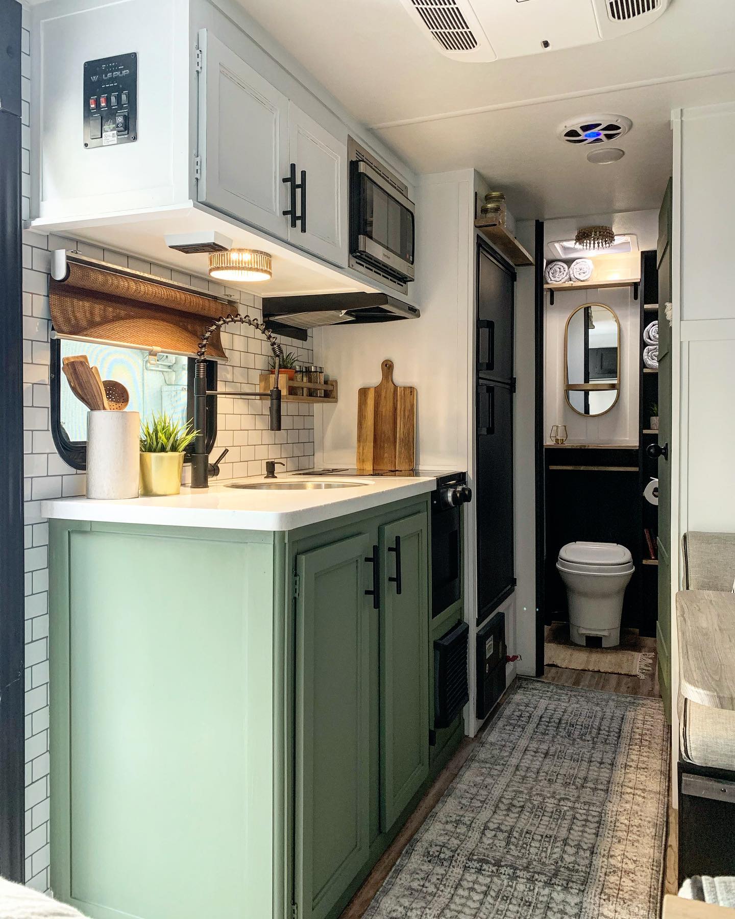 Tiny house kitchen with terracotta red lower cabinets, butcher block counters, open wood shelves with cast iron pans and plants, a gas range, white shiplap walls, and a lofted bed visible above