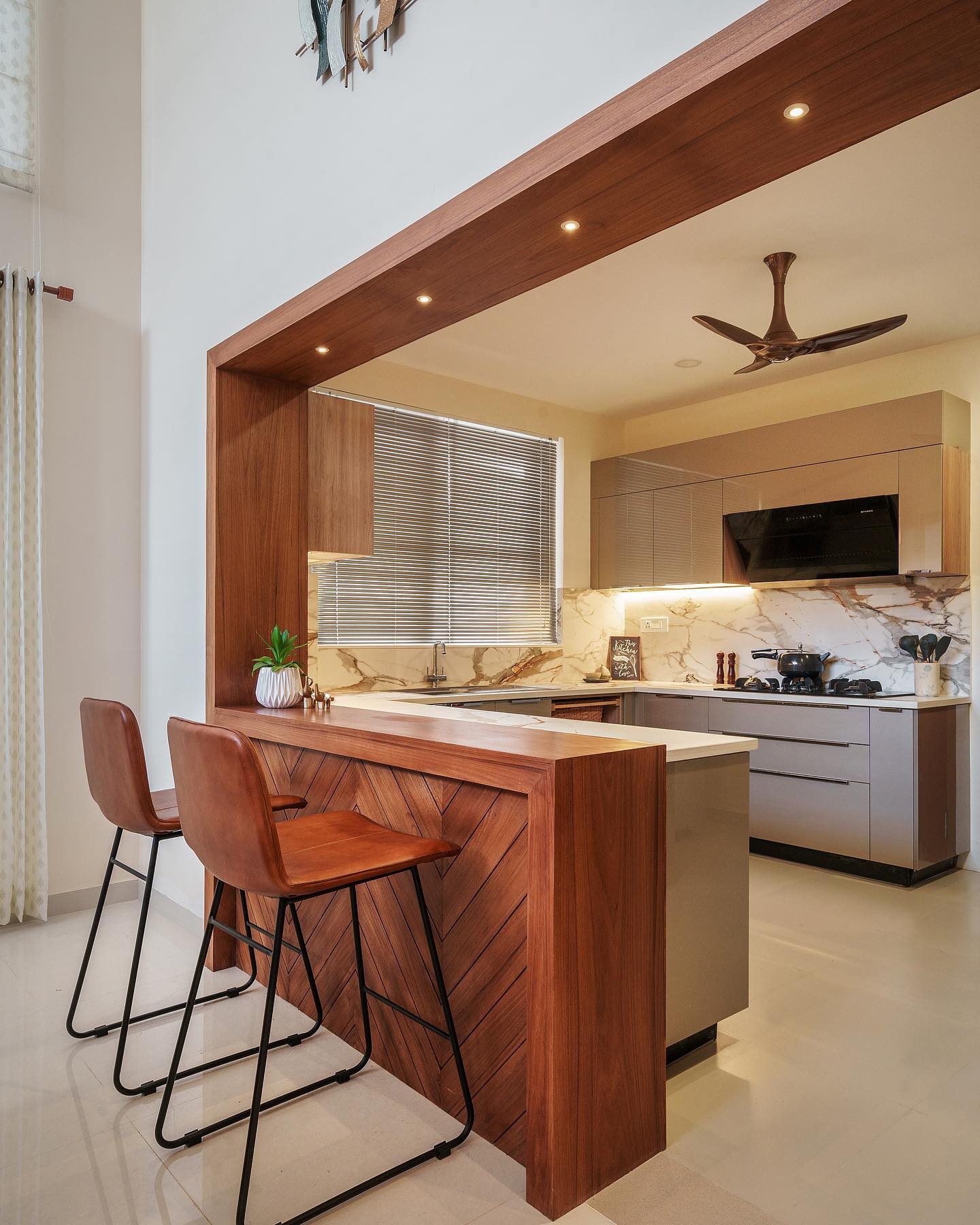 Chunky walnut frame around an open kitchen opening with two leather bar stools, a chevron wood counter front, and a marble backsplash behind the stove