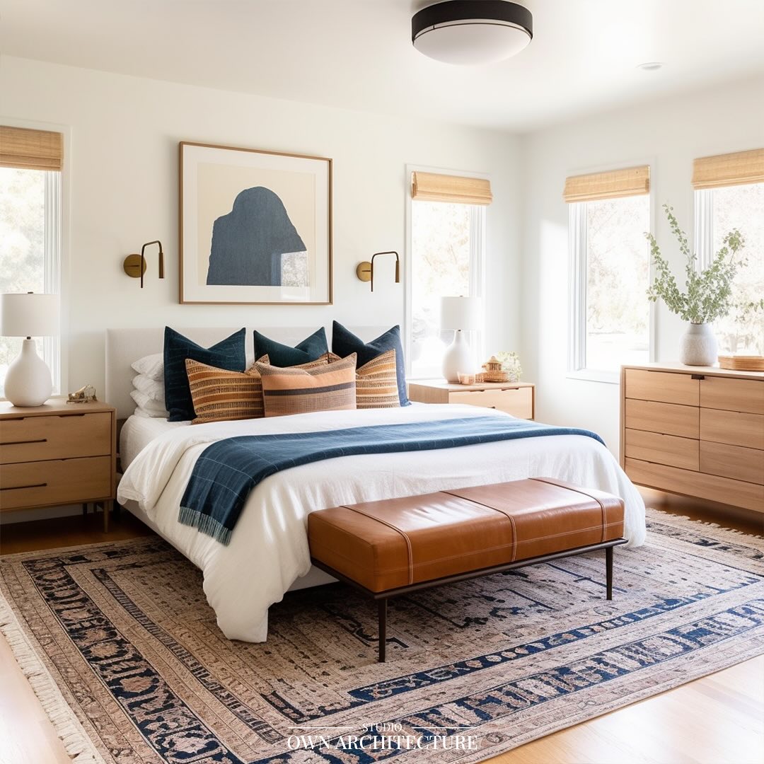 Bright white master bedroom with three windows, indigo and rust striped pillows, caramel leather bench and large vintage navy and tan rug