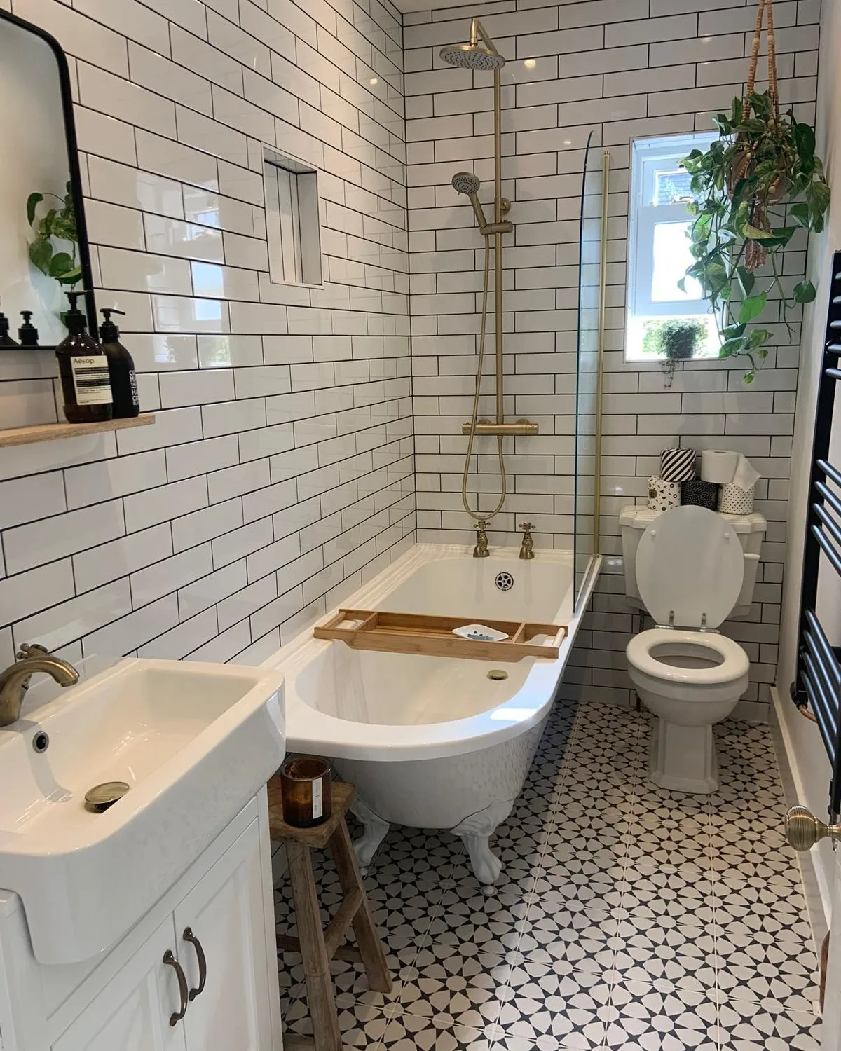 er on exposed piping, brass handheld shower, black and white star-pattern floor tile, slim white console sink and a hanging plant by the window